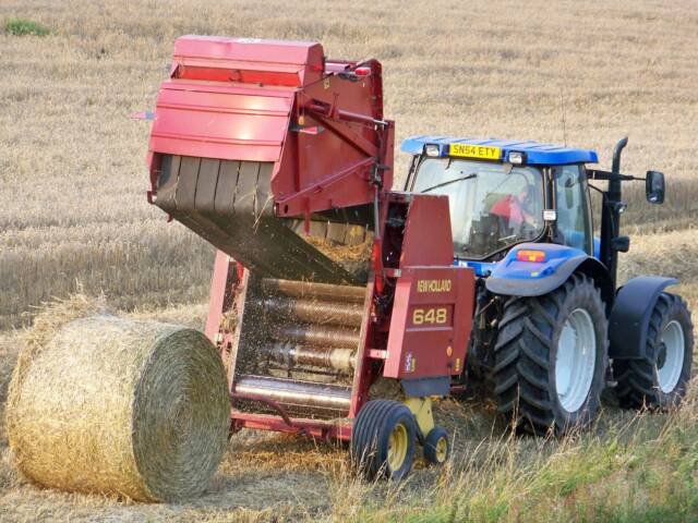 Tractor pulling a round baler as it drops a finished bale
